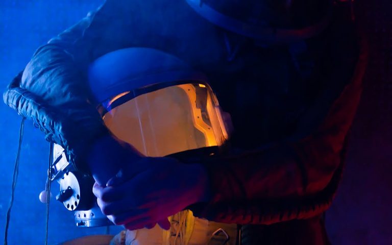 Close-up of an astronaut holding a helmet, enveloped in a dim, colorful light.
