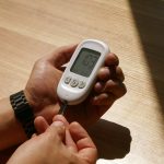 Designing Self-Evolving Bioelectronic Control Platforms Close-up of a person checking blood glucose level with a meter in a sunny room, hands visible.