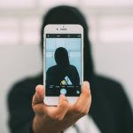 A person in a hoodie takes a mysterious selfie with a smartphone.