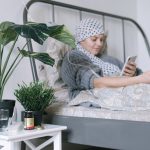 Self-Healing Hospital at Home: Synthetic Media & AI Strategy A woman undergoing cancer treatment relaxes in bed using her phone, surrounded by plants.