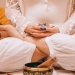 Woman in meditation holding crystal, seated in lotus position with a Tibetan singing bowl, promoting relaxation.