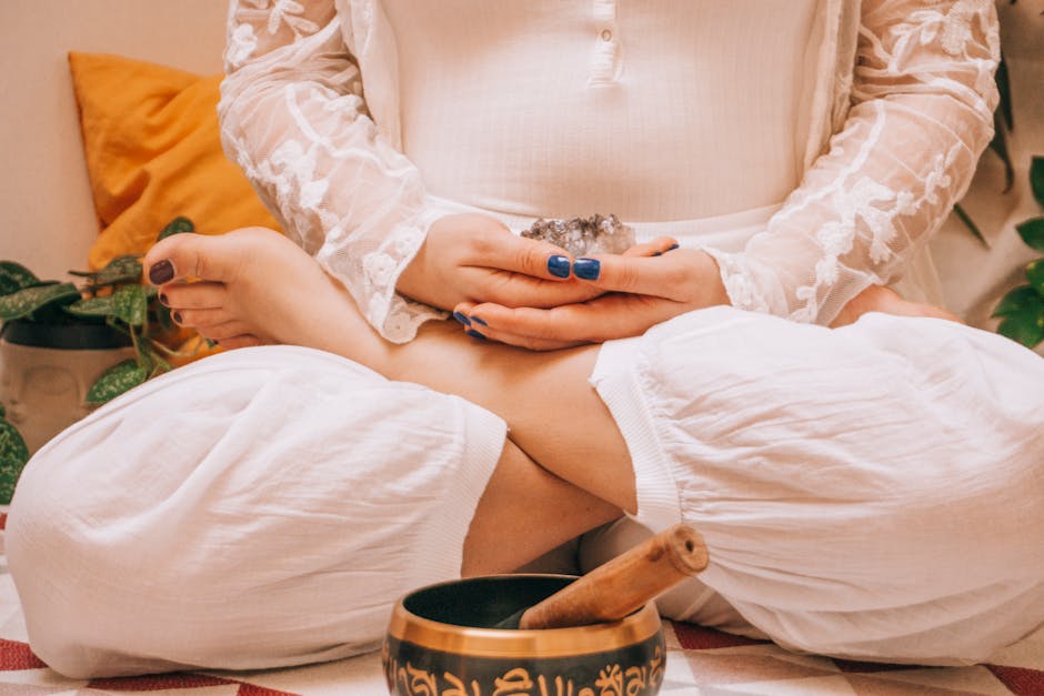 Woman in meditation holding crystal, seated in lotus position with a Tibetan singing bowl, promoting relaxation.