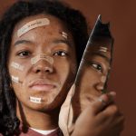 A powerful portrait of a woman embracing imperfections with positive messages on her face, holding a broken mirror.