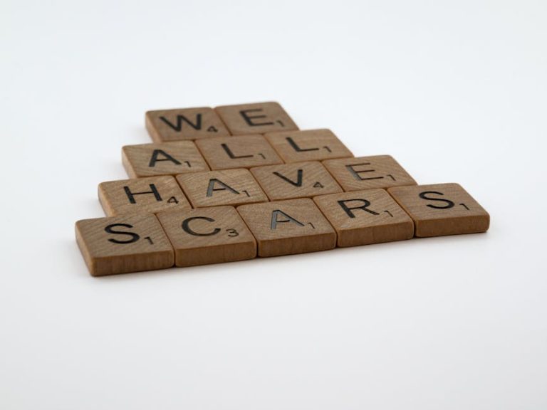 Wooden letter tiles arranged to spell 'we all have scars' on a white background.