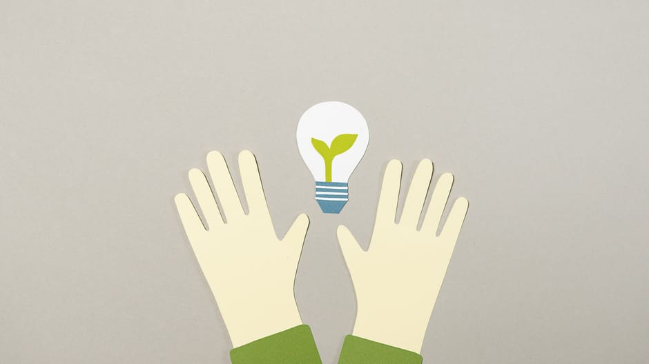 Illustrative paper cutouts featuring hands and a light bulb with a plant, symbolizing environmental awareness.