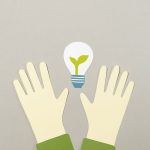 Illustrative paper cutouts featuring hands and a light bulb with a plant, symbolizing environmental awareness.