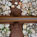 Rusty railway track close-up with gravel stones and greenery.