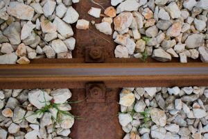 Rusty railway track close-up with gravel stones and greenery.