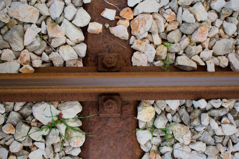 Rusty railway track close-up with gravel stones and greenery.