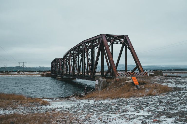 Scenic view of snowy shore against ridges and rippled ocean with aged bridge in wintertime