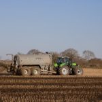 <h1>Symbol-Grounded Synthetic Fertilizers: The Future of Automated Cybersecurity Compilers</h1> A green tractor spreading fertilizer on a brown, freshly plowed farmland under a clear sky.