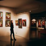 The Aesthetics of Scarcity: How Art Shapes Global Food Security A woman admiring colorful paintings in a contemporary indoor art exhibition.