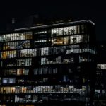 The Architecture of Command: Business as a Lens for Leadership A captivating image of a contemporary office building illuminated against the night sky, showcasing urban architecture.