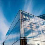 Sleek glass facade reflecting clouds in a modern architectural design under a bright blue sky.