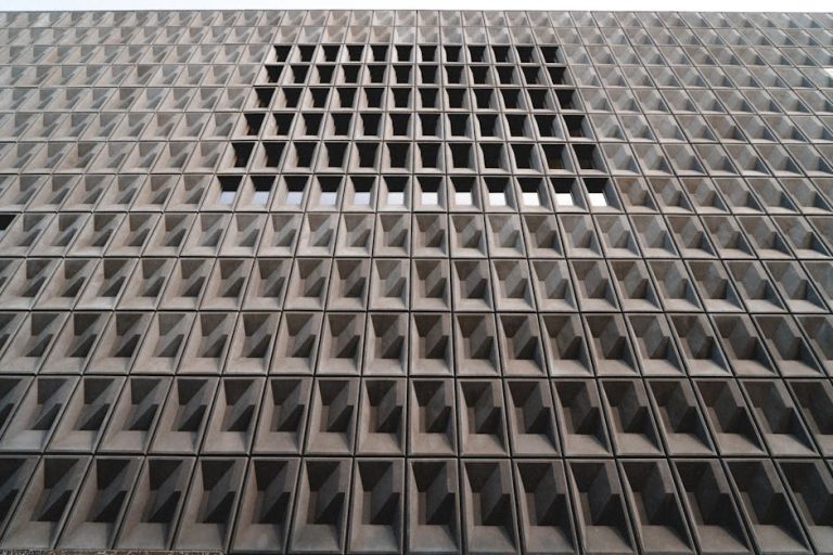 Concrete building facade with geometric patterns and recessed windows, showcasing modern architecture.