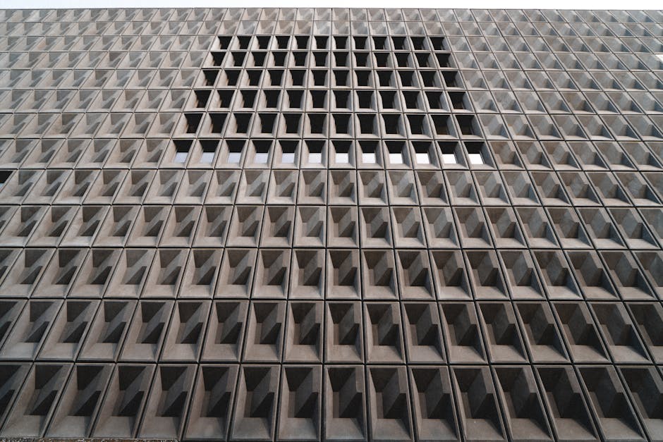 Concrete building facade with geometric patterns and recessed windows, showcasing modern architecture.