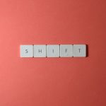 Close-up of keyboard keys spelling 'shift' on a plain red surface.