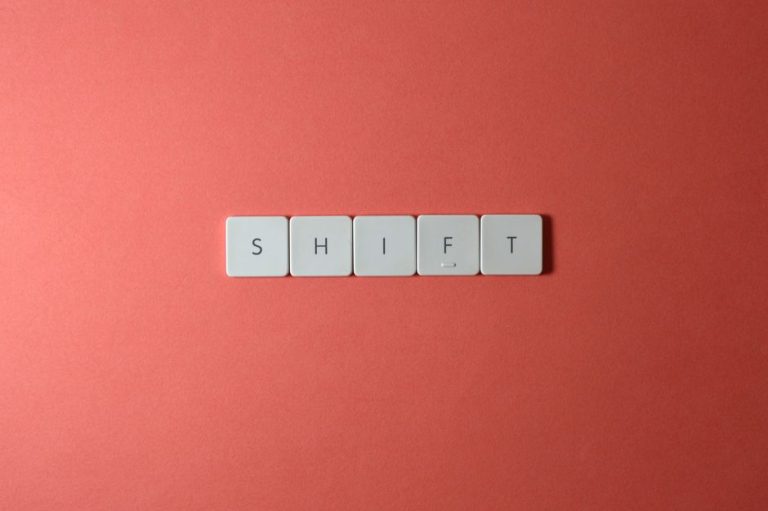 Close-up of keyboard keys spelling 'shift' on a plain red surface.
