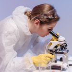 The Biological Edge: Why Health is a Strategic Asset for Leaders Laboratory scientist in protective gear examining samples with a microscope.