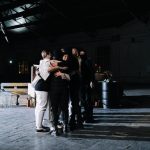 A diverse group of adults embracing in a dimly lit industrial space, symbolizing unity.