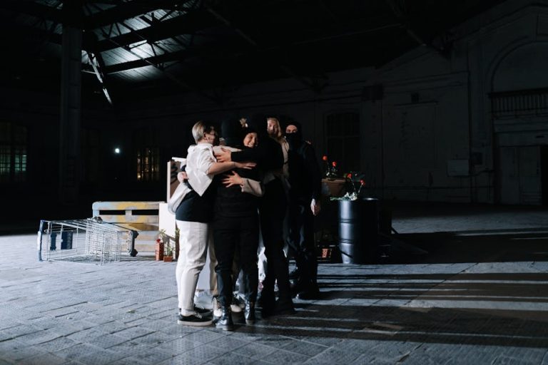 A diverse group of adults embracing in a dimly lit industrial space, symbolizing unity.