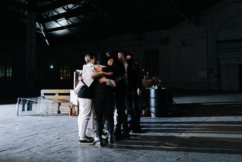 A diverse group of adults embracing in a dimly lit industrial space, symbolizing unity.