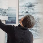 The Curator Economy: How Modern Leadership Redefines Artistic Value A woman arranges abstract art pieces on a gallery wall, showcasing modern creativity.