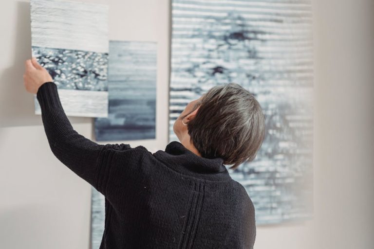 A woman arranges abstract art pieces on a gallery wall, showcasing modern creativity.
