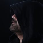 Side view of a bearded man in a hood, creating a mysterious and moody portrait in a studio setting.