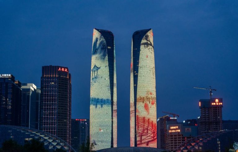 Night view of illuminated skyscrapers with artistic projections in a city skyline.