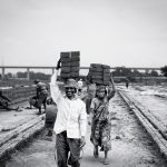 The Economic Architecture of Human Behavior Black and white photo of laborers carrying bricks, depicting hard work and industry.
