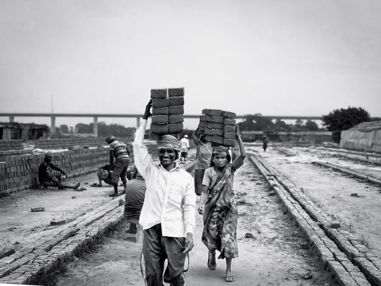 Black and white photo of laborers carrying bricks, depicting hard work and industry.