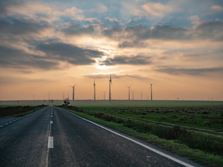 A picturesque rural road leading to wind turbines under a vibrant sunset in Romania, emphasizing renewable energy.