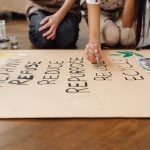 Hands painting on a poster with sustainable message during a school project.