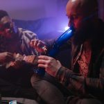 The Economics of Addiction: Music Industry Strategies for Engagement Two friends enjoying music and smoking indoors, capturing a relaxed atmosphere with a musical instrument and smoke.