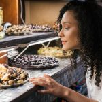 A woman observes a display filled with a variety of olives and other foods.