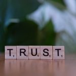 The Economics of Trust: Why Integrity is a Strategic Asset Wooden letter tiles spelling TRUST on a wooden surface, symbolizing integrity and values.