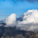 Fluffy clouds float over the rugged alpine mountains, creating a dramatic natural scene.