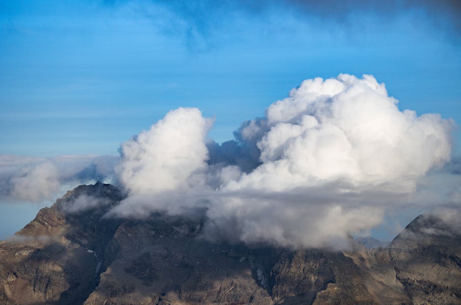 Fluffy clouds float over the rugged alpine mountains, creating a dramatic natural scene.