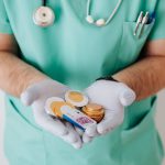 Unrecognizable medical worker demonstrating money wearing medicine form standing near white wall in hospital while working in day of salary