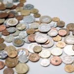 The Ethical Cost of Global Health: Strategic Trade Dilemmas A diverse collection of international coins spread across a white surface, showcasing various currencies and designs.