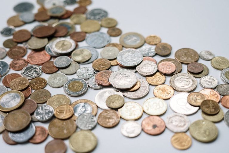 A diverse collection of international coins spread across a white surface, showcasing various currencies and designs.