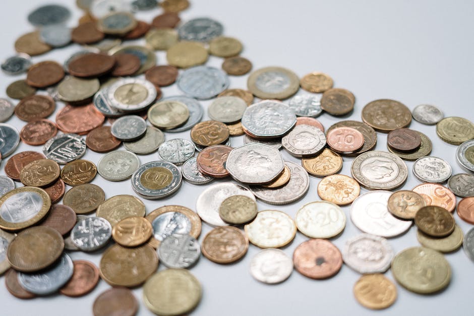 A diverse collection of international coins spread across a white surface, showcasing various currencies and designs.