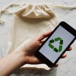 From above view of crop person holding smartphone with recycling symbol on screen and white textile bag placed on marble table