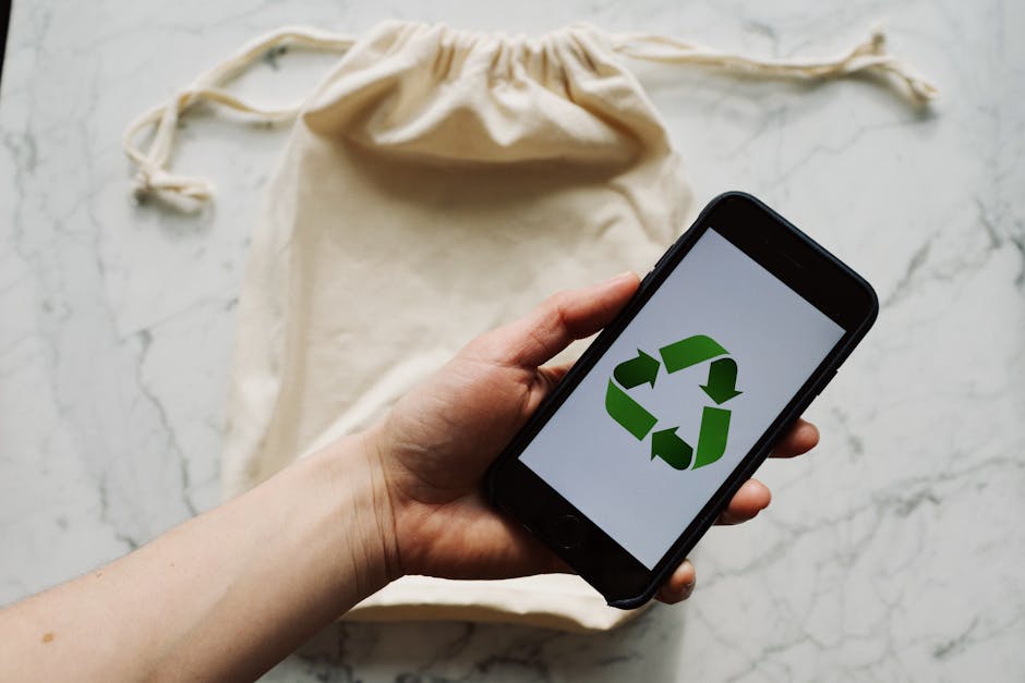From above view of crop person holding smartphone with recycling symbol on screen and white textile bag placed on marble table