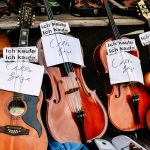 The Evolution of Music Trade: From Physical Assets to Digital Streams A collection of vintage string instruments on display at an outdoor market with purchase signs.