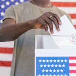 A person casting their vote at a polling station with a US flag in the background.
