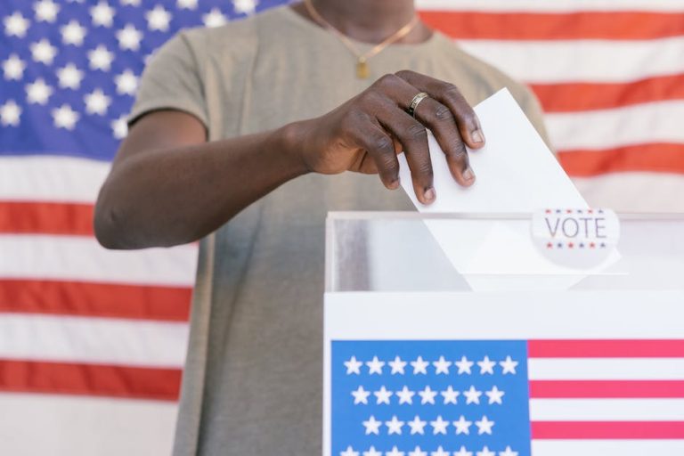 A person casting their vote at a polling station with a US flag in the background.