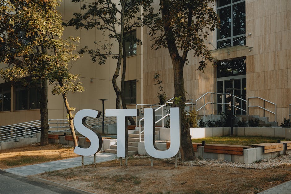 Modern building entrance with large STU letters surrounded by greenery and urban design.