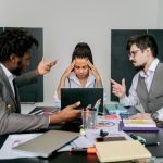 The Future of Business Conflict: Asymmetric Warfare and Strategy Two men argue while a woman looks frustrated at a laptop in an office environment.